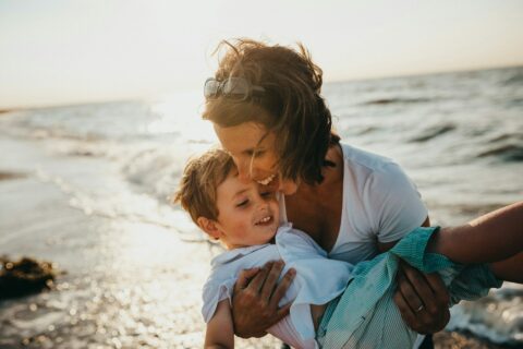 Bild zeigt Mama am Strand mit Kind in den Armen / Mama Sprüche zum Weinen